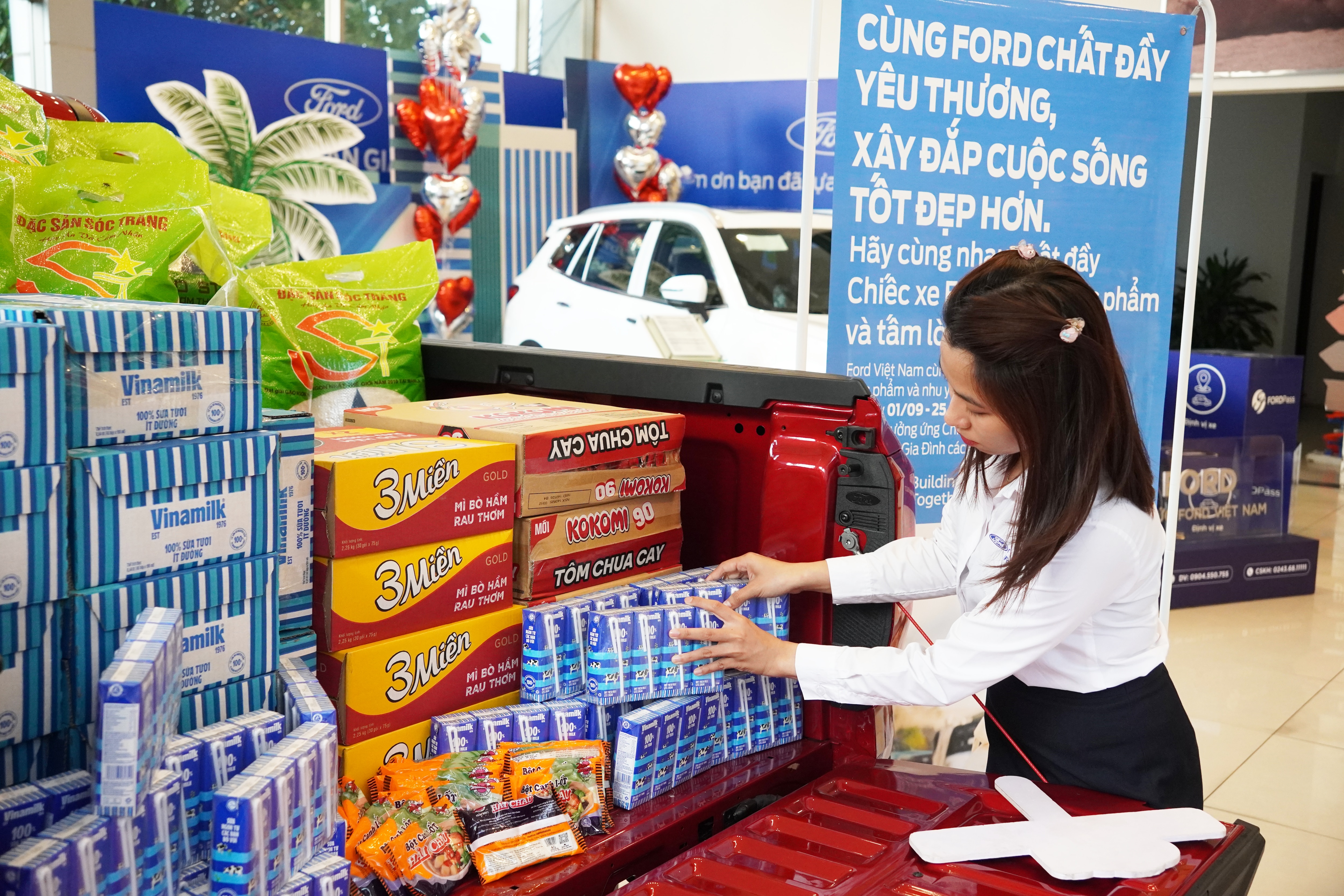 A woman helps stack donated food items at a food donation event in a Ford dealership.